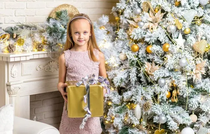 bambina tiene in mano un regalo di natale in una stanza con addobbi natalizi