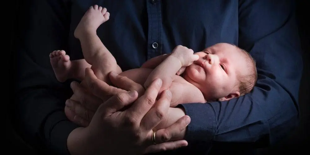 neonato tenuto tra le braccia del padre