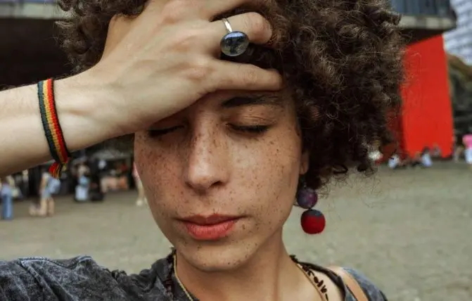 donna con capelli ricci e con la pelle lentigginosa si tocca la testa sofferente