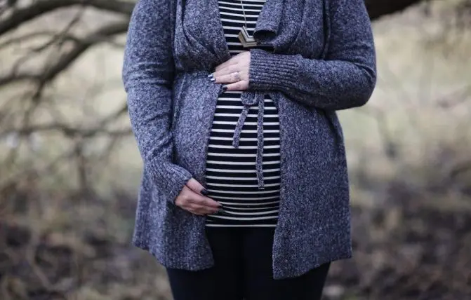 donna con maglietta a righe bianche e nere e cardigan si tocca il pancione