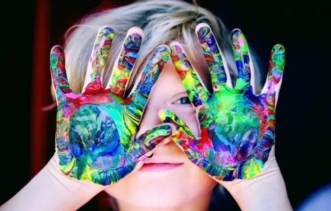 bambino mostra i palmi delle mani macchiate di diversi colori