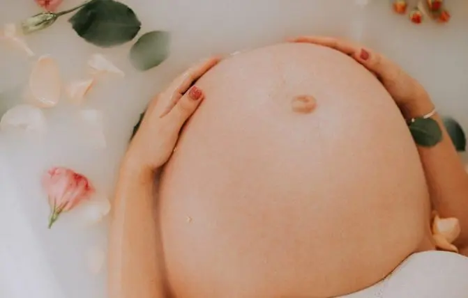 donna tocca la pancia al nono mese di gravidanza in una vasca con fiori e foglie