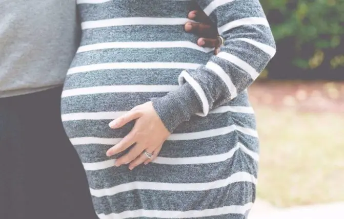 donna in gravidanza abbraccia il compagno e indossa un vestito a righe bianche e grigie