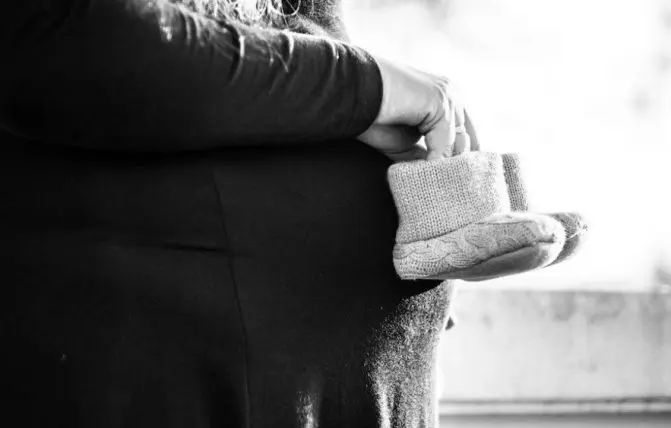 immagine in bianco e nero di donna in gravidanza che tiene davanti il pancione scarpine da neonato