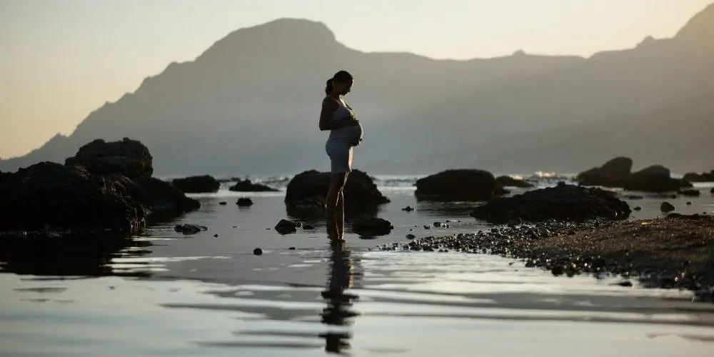 donna in gravidanza sta in piedi nel bagnasciuga con i piedi in acqua
