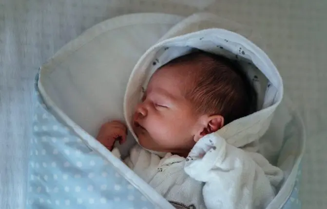 neonato dorme avvolto in una coperta azzurra a pois bianchi